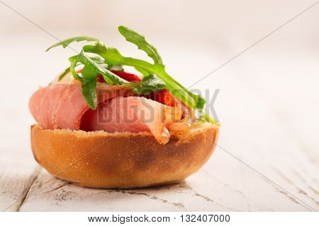 Sandwich with duck breast and arugula on a white wooden table