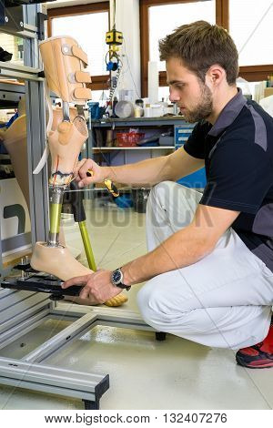 Young bearded man working on shin and knee section on prosthetic leg assembly in laboratory for research and development