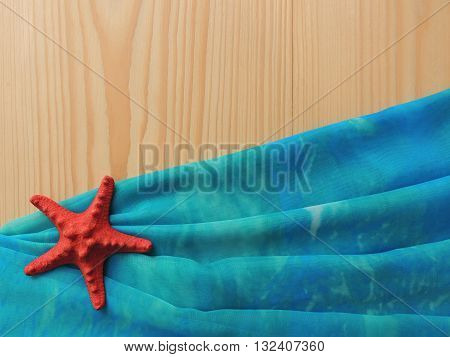 Blue pareo textile folds on wooden background with red starfish.