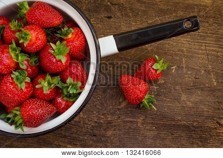 White metal colander filled with succulent juicy fresh ripe red strawberries on an old wooden textured table top. Background from freshly harvested strawberries. Directly above. Top view. Horizontal.