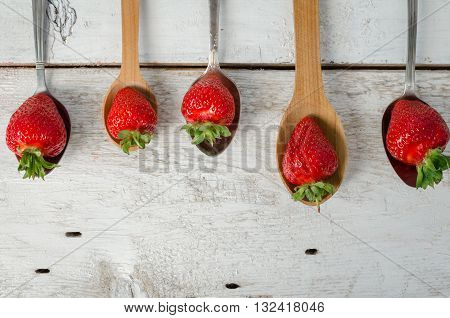 Succulent juicy fresh ripe red strawberries on vintage metal and wooden spoons over white rustic table. Agriculture Gardening Harvest Concept. Background with space for text. Top view. Copy space.