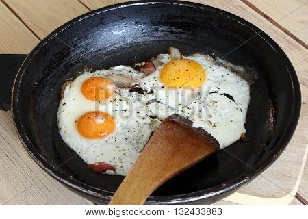 Detail of the fried eggs with bacon on the pan - a hearty breakfast - home cooking