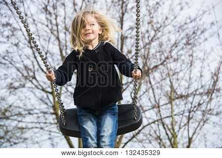 Little child blond girl having fun on a swing outdoor. Summer playground. Girl swinging high