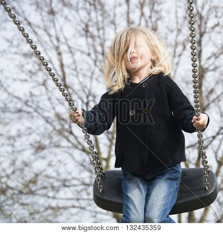 Little child blond girl having fun on a swing outdoor. Summer playground. Girl swinging high