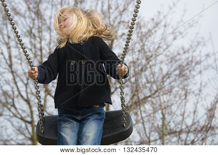 Little child blond girl having fun on a swing outdoor. Summer playground. Girl swinging high