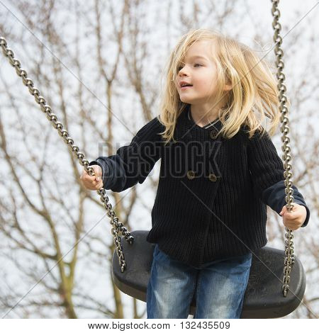 Little child blond girl having fun on a swing outdoor. Summer playground. Girl swinging high