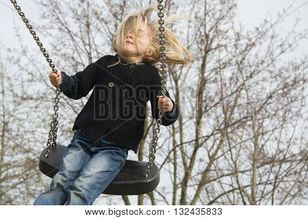 Little child blond girl having fun on a swing outdoor. Summer playground. Girl swinging high