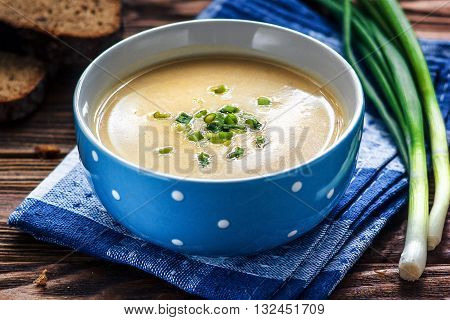 Homemade vichyssoise cream soup served with chives, in blue bowl on wooden table.