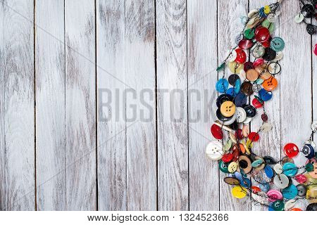 Handmade bright colored jewelry made of plastic buttons on the white wooden background. Place for text.