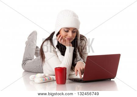 Beautiful young  woman in winter clothes with laptop lies on a white background.
