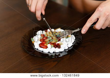 The plate with nutritional supplements standing on the kitchen table, female hands hold fork and knife.