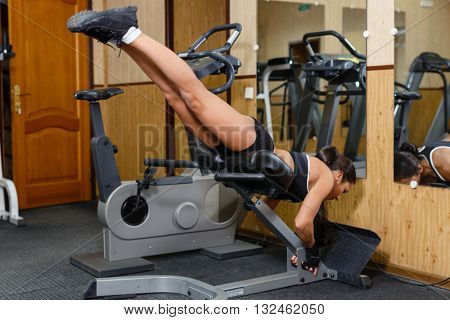 Sports young woman doing exercises on  trainer back machine in the gym. Reverse Hyperextension.
