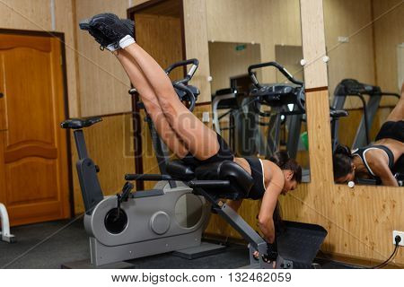Sports young woman doing exercises on  trainer back machine in the gym. Reverse Hyperextension.