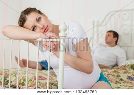 The pregnant woman becomes angry about the husband who lies on a bed and watches TV.