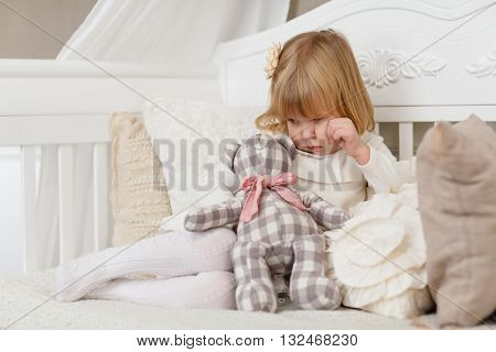 Sad pretty girl with toy bear sits on a sofa in the room.