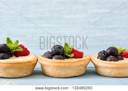 Delicious tartlets with raspberries and blueberries on blue background