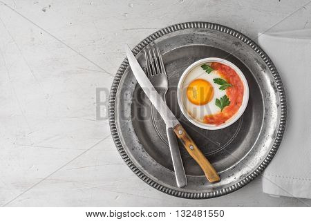 Eggs baked with tomatoes and parsley in the ramekins with cutlery top view