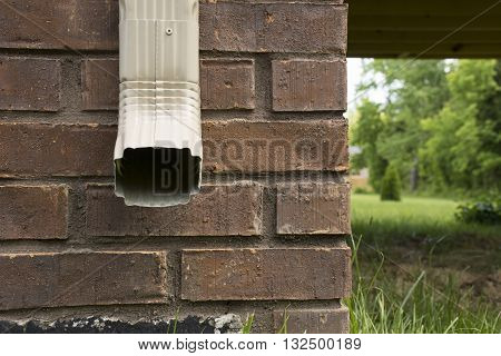 Downspout of a rain gutter against the side of a house facing forward.