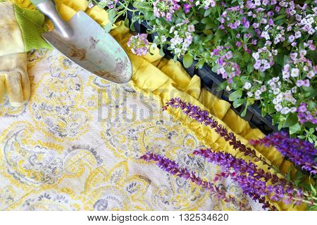 A set of Garden tools including shovel work gloves and Sweet Alyssum Flowers are framing pretty yellow fabric of a woman's apron background for copy-space.