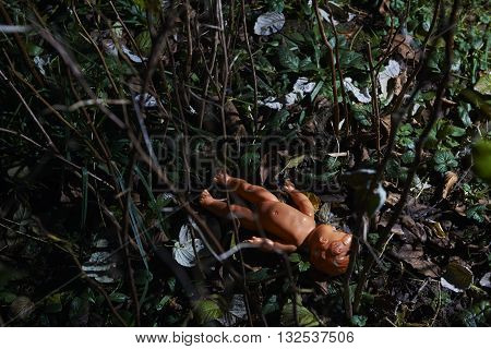 Scary doll lying at dark forest. Conceptual scene of child abuse. Crime scene.