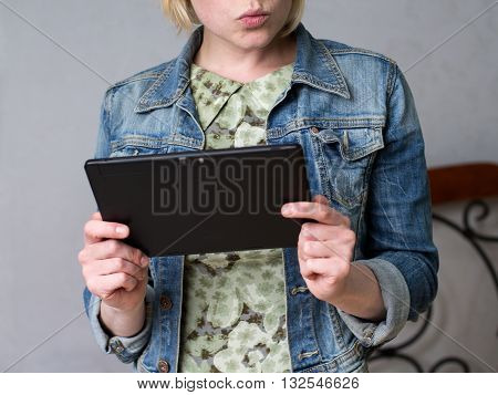 Close up young blonde woman holding a tablet and smiling looking at the screen