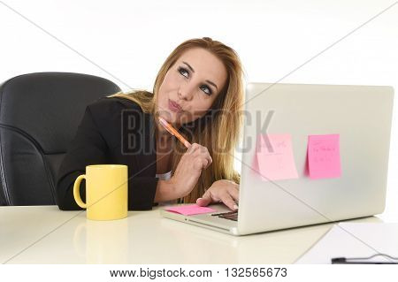 attractive 40s blond businesswoman working at office laptop computer sitting on the desk absent minded and thoughtful smiling happy as if thinking of vacation isolated on white background