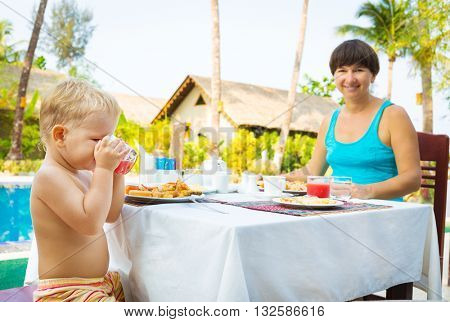 Child with mother have a breakfast near a swimming pool. Focus on a child