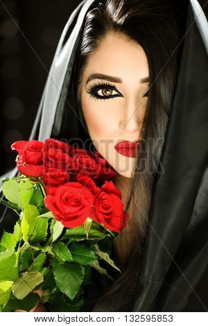 Portrait of a beautiful female model holding red roses and a black veil with red lips