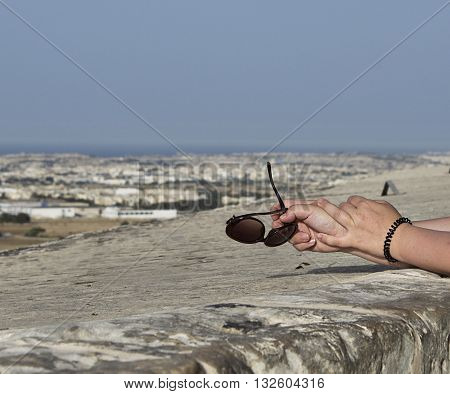 Woman keeping sunglasses in her hands with the panoramic view to Malta island, view from Mdina city, Malta, body part, conceptual photo of summer holidays