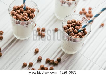 Chocolate cereal balls with milk in glasses on white wooden background