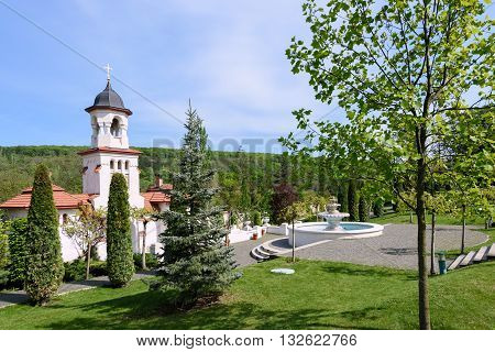 Bell tower and basin at orthodox Curchi monastery in Moldova with green trees and blue sky