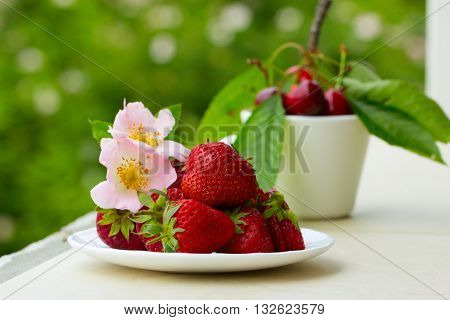 Group of fresh spring fruits together cherries and strawberries. Cherries in white bowl.Strawberry on a wooden background. Red strawberries. Strawberries on green