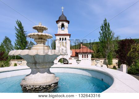 Bell tower and basin at orthodox Curchi monastery in Moldova with green trees and blue sky
