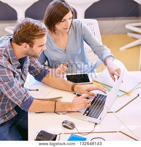 male and female business partners working together early in the morning on a laptop and tablet in a public co-working space