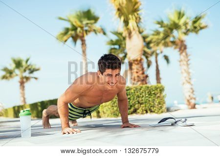 Handsome man doing push ups on the beach.
