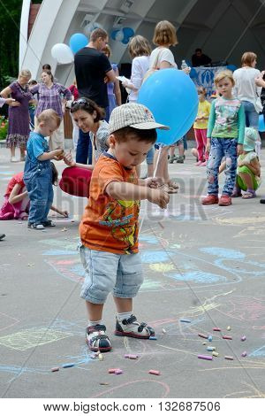 KHARKOV UKRAINE - 20 JUNE 2015: World Refugee Day observed in Kharkov Ukraine. A little boy with a blue baloon playing with colorful pieces of chalk.