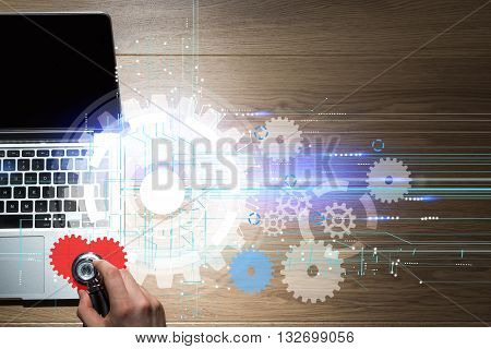 Computer repair service with hand listening to abstract laptop heartbeat with digital cogweel pattern on wooden desktop