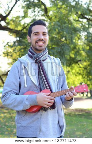 Portrait of young handsome man playing the ukelele in a park. Outdoors.