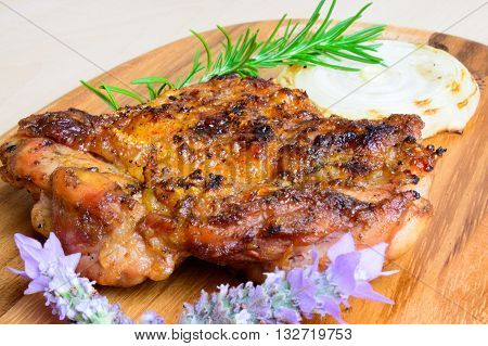 barbecued grilled boneless chicken thigh and grilled onion slice with fresh rosemary and lavender garnish on a plank board and neutral background