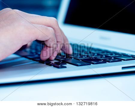 Woman hand typing on laptop keyboard. Hand with laptop typing in blue color tone. Selective focus.