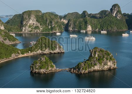 Distant View of the lush green covered limestone karsts formation on Ha Long Bay in Vietnam. The clear blue sky looks gorgeous. Tourist boats are seen sailing on the blue water.