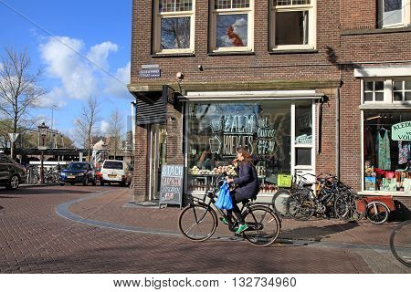 AMSTERDAM, NETHERLANDS - MAY 3, 2016: Local woman on bicycle in historical center in Amsterdam, the Netherlands. Bicycles outnumber the people in Amsterdam: 760000 citizens and nearly a million bikes.
