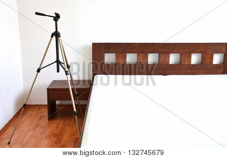 Tripod for camera next to the wooden bed in bedroom