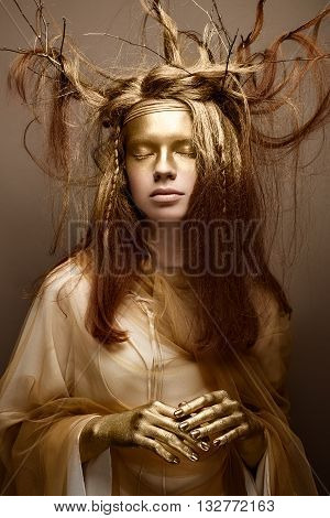 Beautiful girl in the image of a tree with branches in her hair. The model with creative make-up. The photo was taken in a studio. Beautiful face.