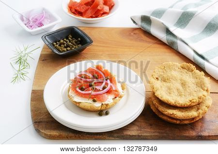 Healthy home made gluten free biscuit with smoked salmon lox cream cheese capers and red onion slices on white plate in horizontal format