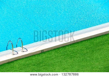 Infinity pool on the bright summer day with green grass around.Swimming pool with stairs into the water.Hotel swimming pool with sunny reflections close up view.