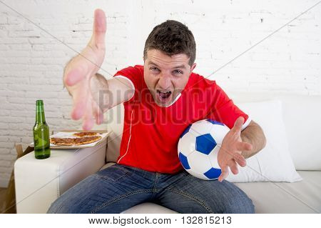 young supporter man with ball and beer bottle watching football game on television sitting at home couch in stress dejected and disappointed for failure shouting and complaining