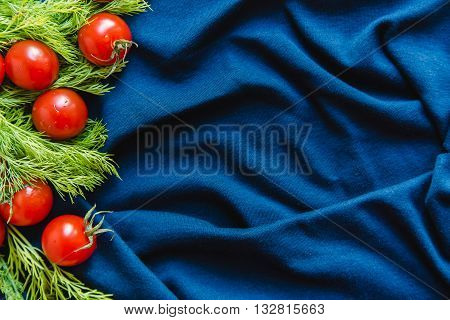 Top view of appetizing cherry tomatoes and dill over blue textile background copy space