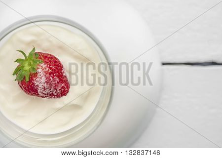 Single strawberry with sugar, cream or yogurt as a sweet dessert in glasses ball on wooden light blue table
