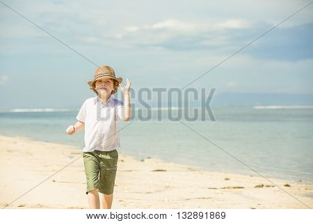 Happy caucasian boy with red hair in hat enjoing summer on tropical beach